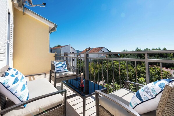 A balcony with wicker furniture, a glass table, and a view of neighboring houses.