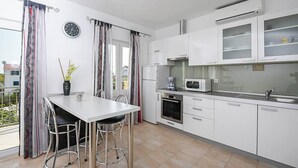 A modern kitchen with white cabinets, a microwave, and a stove. There is a dining table with chairs and a clock on the wall.