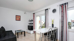 A modern living room with a sofa, a small table, a TV, and a dining area with a white table and metal chairs.