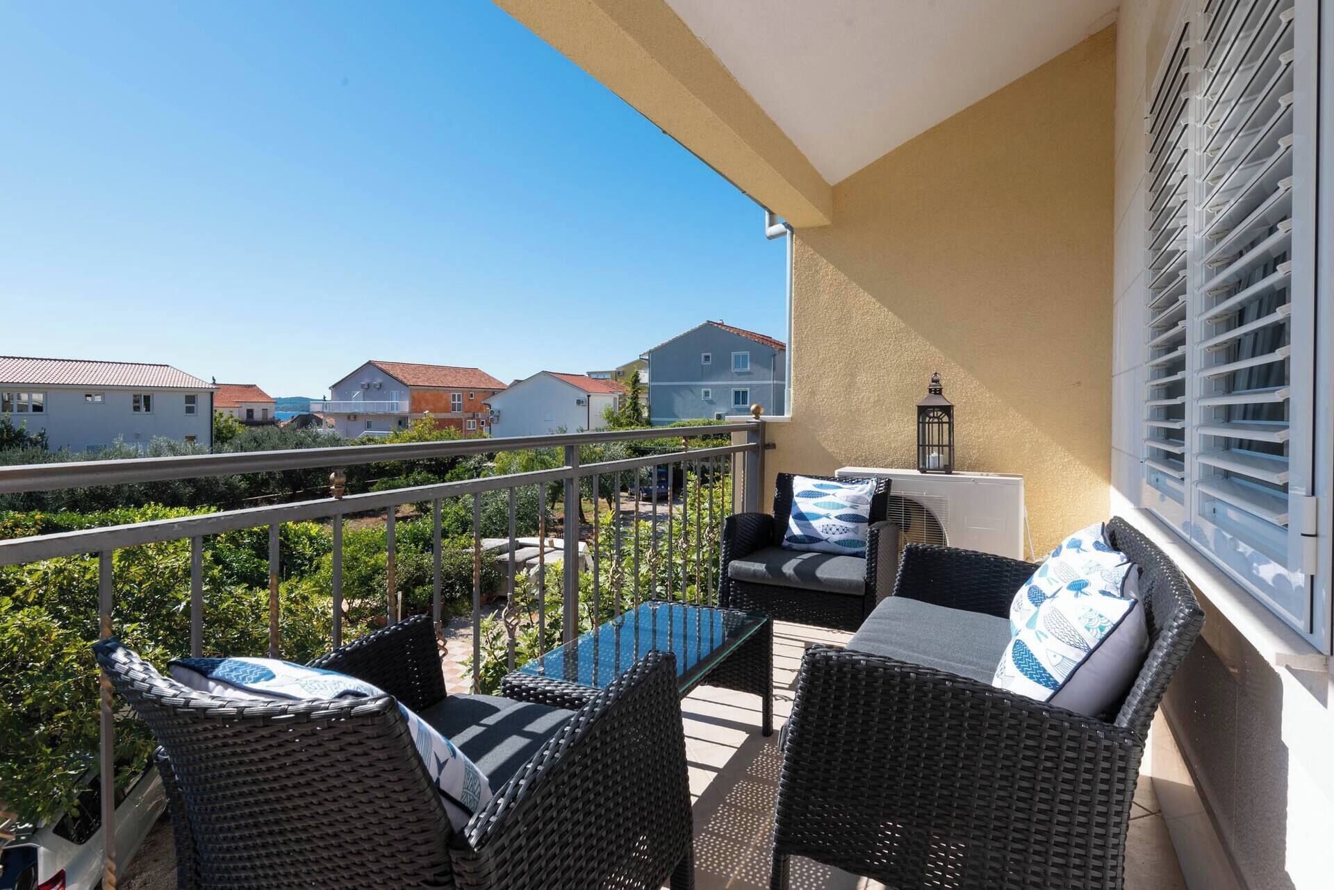 A balcony with wicker furniture, a table, and a view of neighboring houses.