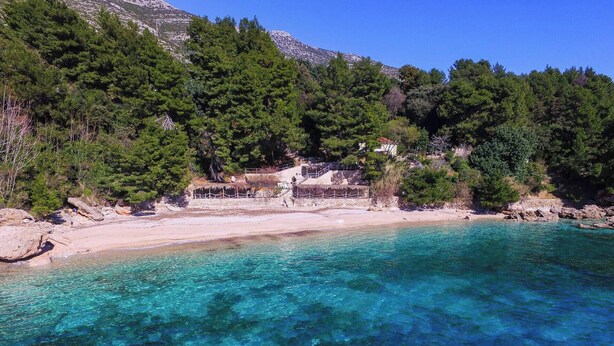 A beach with clear turquoise water, rocky shoreline, and dense green forest in the background. - 2-Bedroom Apartment Mokalo with amazing sea view! (Orebic)