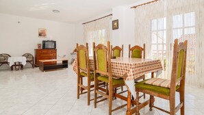 A dining area with a table set for six, surrounded by wooden chairs with green upholstery. A wooden cabinet and a television are visible in the background. - Great 2-Bedroom Apartment for up to 6 persons (Orebic)