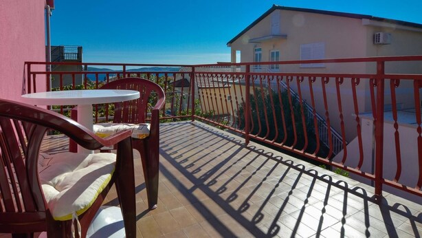 A balcony with a table and chairs, a red railing, and a view of a building and the sea. - Great 2-Bedroom Apartment for up to 6 persons (Orebic)