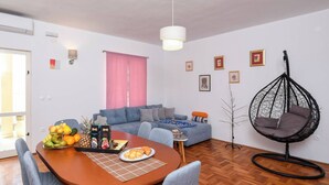 A modern living room with a dining table, grey sofa, hanging chair, and a large window with pink curtains.
