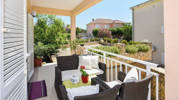 A balcony with wicker furniture, a potted plant, and a view of neighboring houses and greenery.