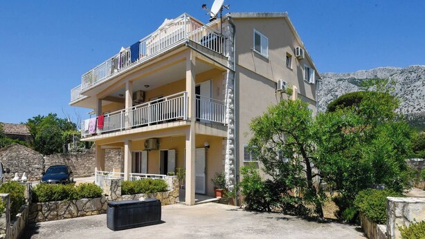 A two-story building with balconies, a stone wall, and a parked car. - Beautiful 1-Bedroom Apartment Sandra (Orebic)