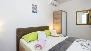 A neatly made bed with pillows and a blanket, a bedside lamp, a wall-mounted air conditioner, a framed picture, and a mirror. - Beautiful 1-Bedroom Apartment Sandra (Orebic)