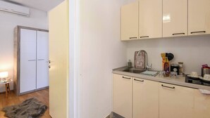 A small, modern kitchen with white cabinets, a stainless steel sink, and a small countertop. There is a door leading to another room, and a fur rug on the floor. - Beautiful 1-Bedroom Apartment Sandra (Orebic)