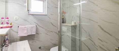 Un baño con cabina de ducha de vidrio, inodoro blanco y lavamanos con espejo.