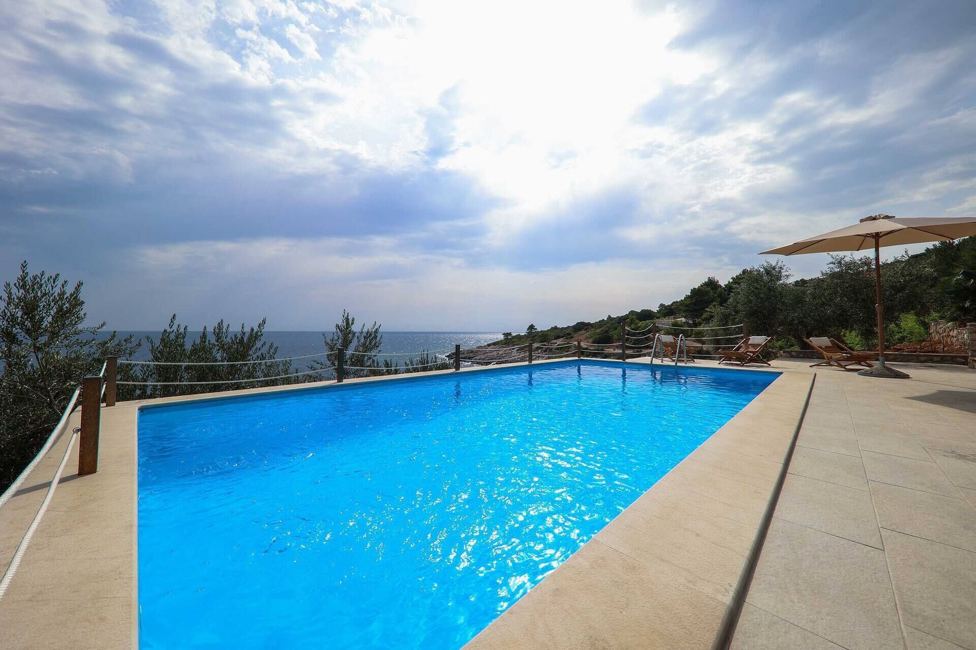 Ein rechteckiger Swimmingpool mit klarem, blauem Wasser, umgeben von einer Holzterrasse und Liegestühlen.