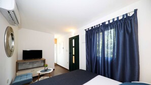 Een slaapkamer met een bed, een televisie op een standaard, een tafeltje met een vaas, en een deur naar een andere kamer.