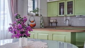 Una cocina moderna con armarios verdes, una mesa de vidrio con un mantel de encaje y un jarrón de flores moradas.