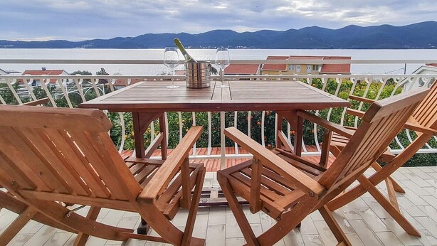 Una mesa y sillas de madera en una terraza con vistas al mar y a las montañas.