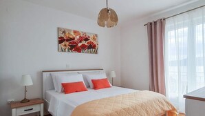 Un dormitorio con cama, mesitas de noche, lámpara, un cuadro y ventana con cortinas.