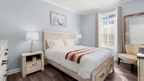 A bedroom with a bed, nightstands, a chair, a dresser, and a window with curtains.