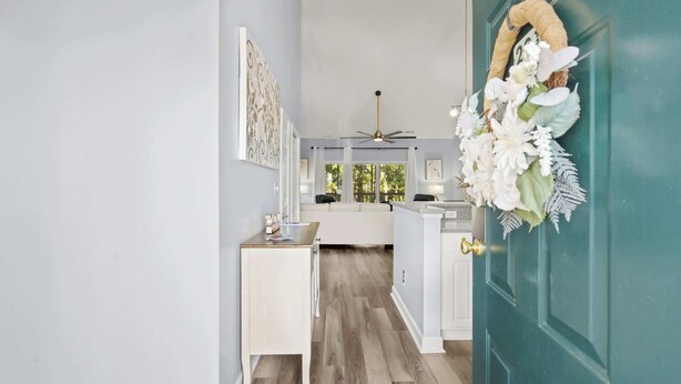 A hallway with a teal door, a white bench, and a ceiling fan.