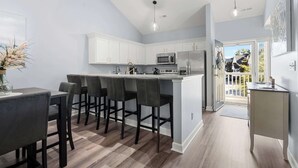A modern kitchen with white cabinets, a large island with bar stools, and a view to the outside.