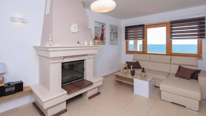 Een woonkamer met een open haard, een bank, een salontafel en uitzicht op zee door grote ramen.