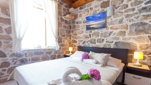 A bedroom with a stone wall, a bed with white linens, two bedside lamps, and a window with curtains. - The Hidden Treasure Village, 7-Bedroom Luxury Holiday Resort with children playground, private Pool and Private Parking, SEA VIEW (Orebic)