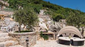 A stone patio with outdoor seating, including a round table and chairs, surrounded by greenery and a stone wall. - The Hidden Treasure Village, 7-Bedroom Luxury Holiday Resort with children playground, private Pool and Private Parking, SEA VIEW (Orebic)