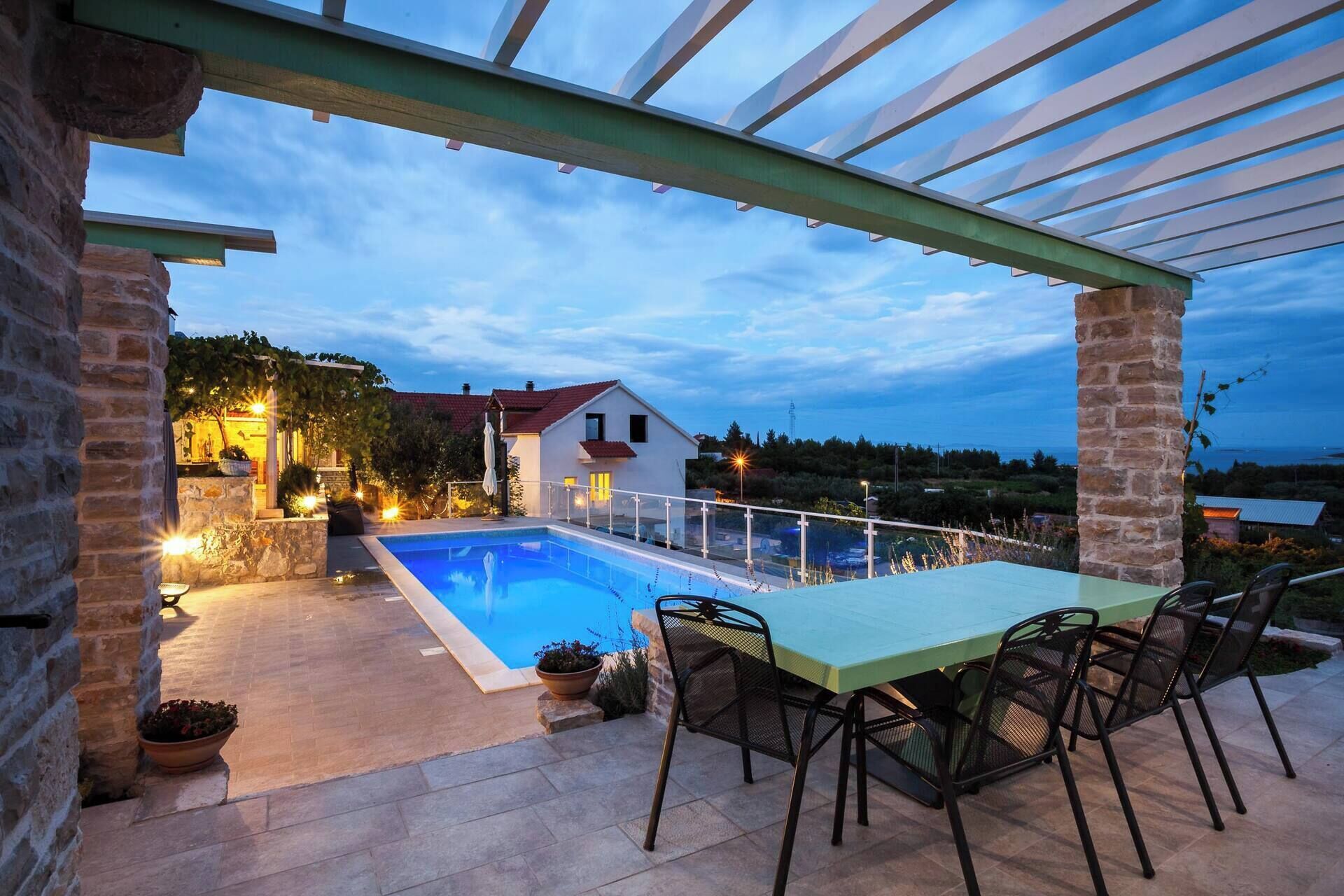 A poolside area with a covered patio, stone walls, and a view of the surrounding landscape.