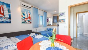 A modern, well-lit room with a bed, a dining table with chairs, and a kitchen area visible through an open door. - Charming Studio Apartment with Sea View (Orebic)