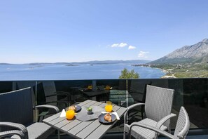Ein Balkon mit einem Frühstückstisch, mit Blick auf die Küste und Berge in der Ferne.