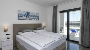 Une chambre d’hôtel moderne avec un grand lit, une table de chevet, une lampe fixée au mur et un tableau représentant des voiliers.