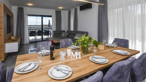 Un espace de repas moderne avec une table en bois dressée pour six personnes, une grande fenêtre avec des rideaux et une vue sur la ville.