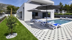 Un bâtiment moderne à deux étages doté d’une piscine, de chaises longues et de parasols.