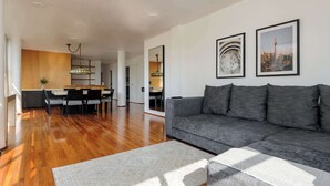 A modern living room with a grey sofa, wooden flooring, and a dining area with chairs and a table.