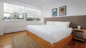 A modern bedroom with a large bed, a view of the city through floor-to-ceiling windows, and two framed pictures on the wall.