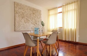 A dining area with a wooden table, four chairs, a large textured wall art piece, a vase with a plant, and a window with curtains. - w* | Comfy 2BR w/ Lovely Deco in Miraflores (Miraflores)