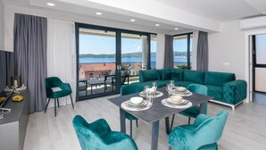 A modern living room with a dining area, large windows, and a view of the sea.