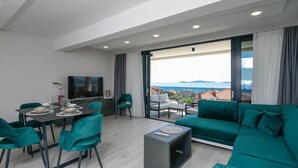 A modern living room with a dining area, a large TV, and a view of the sea.