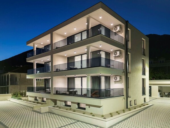 A modern multi-story building with balconies, large windows, and air conditioning units.