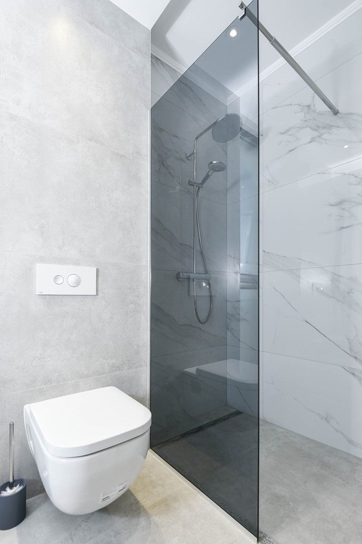 A modern bathroom with a glass-enclosed shower, a white toilet, and a marble-tiled wall.