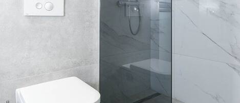 A modern bathroom with a glass-enclosed shower, a white toilet, and a marble-tiled wall.