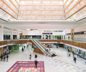 Un centro comercial de varios niveles con escaleras mecánicas, tiendas y un amplio espacio abierto con suelo estampado.