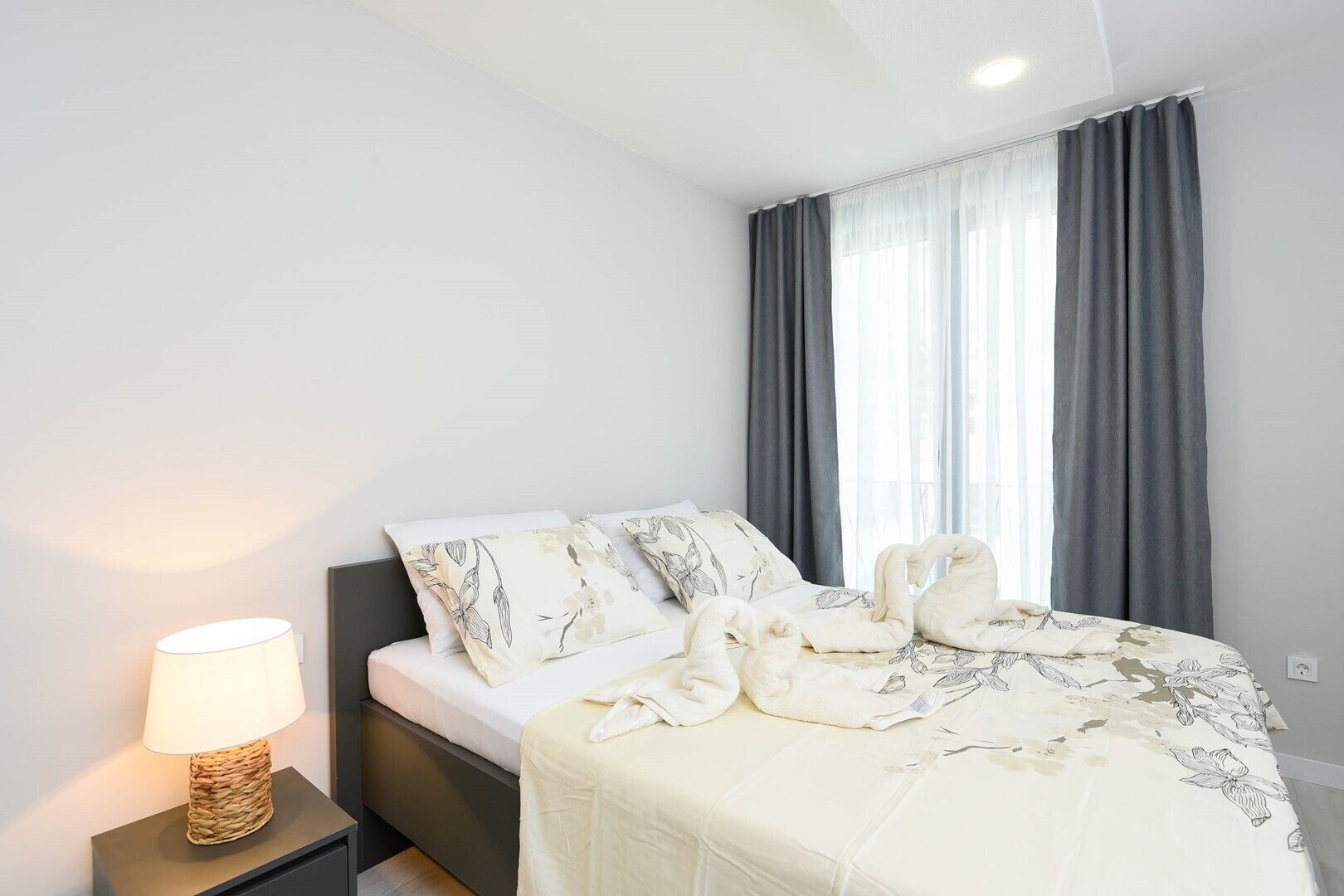 Un dormitorio moderno con cama, lámpara de noche y ventana con cortinas.