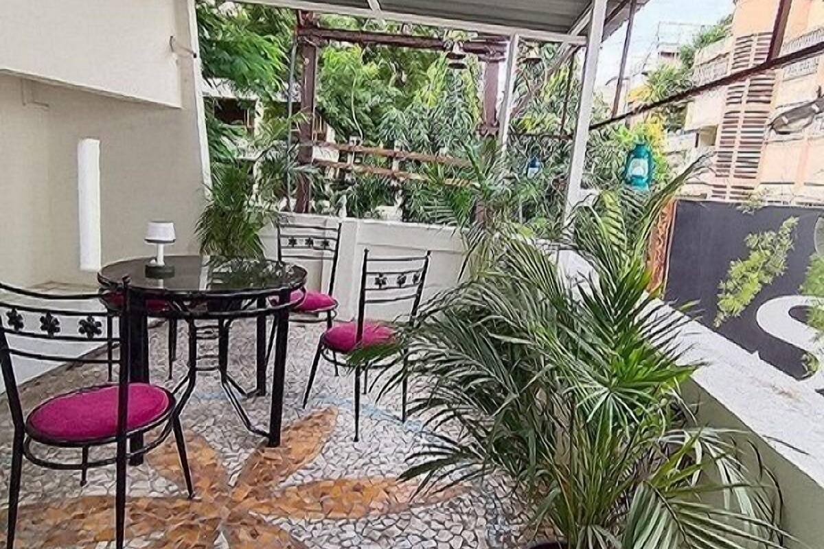 Een overdekt terras met een mozaïekvloer, een tafel met stoelen en potplanten.