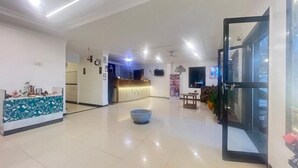 Un vestíbulo amplio con mostrador de recepción, una zona de estar con una silla azul y una puerta de cristal que da al exterior.