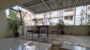 Un espacio al aire libre cubierto con suelo de baldosas, una mesa con sillas y plantas en macetas.