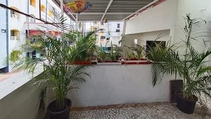 Un espacio al aire libre cubierto con plantas en macetas, suelo de baldosas y una decoración colgante de colores.