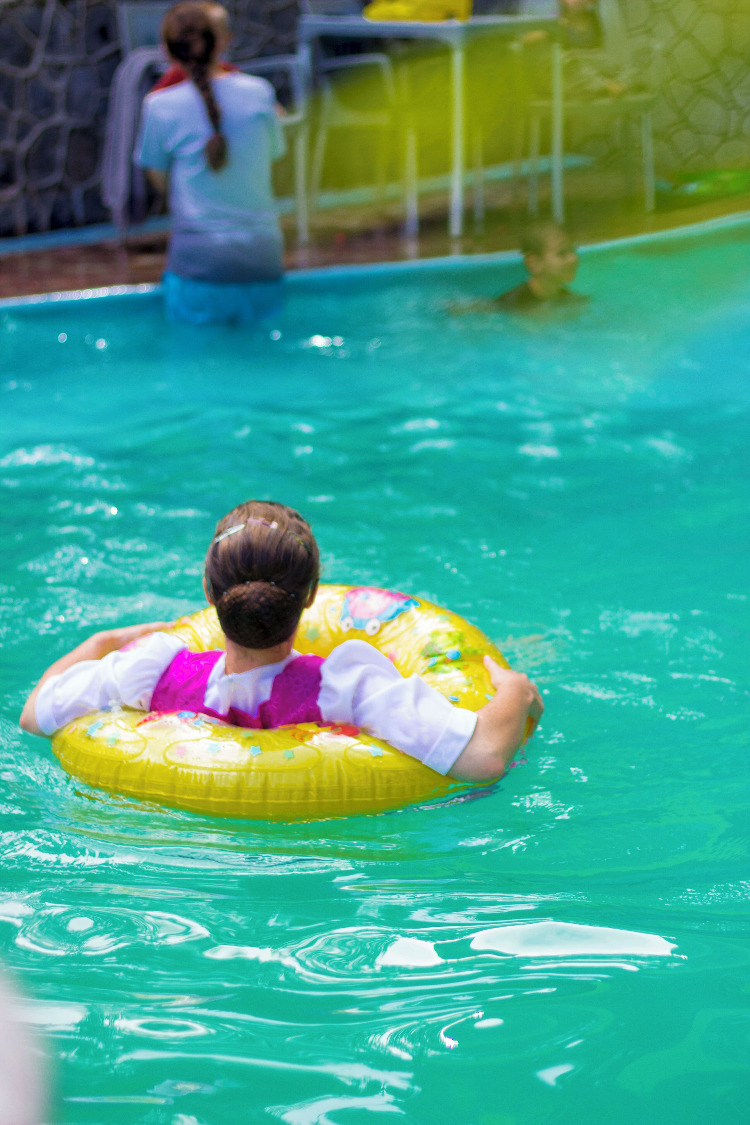 A person floating on a yellow inflatable ring in a pool.
