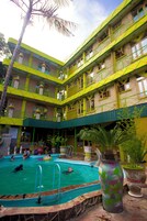 A multi-story hotel with a swimming pool, balconies, and potted plants.