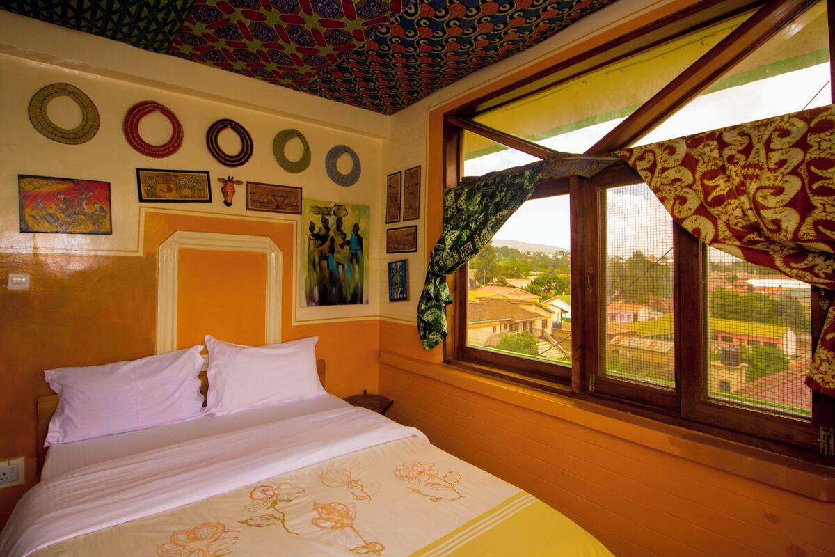 Een kamer met een bed, een raam met uitzicht en verschillende decoraties aan de muur.