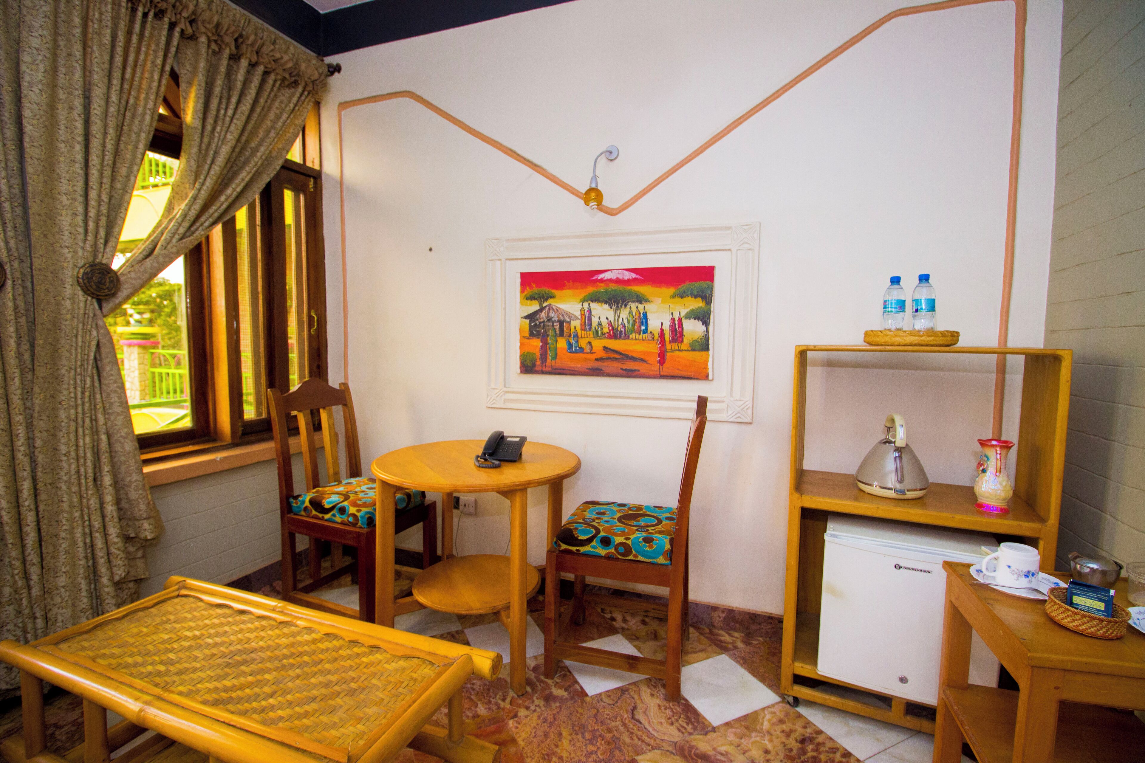 Una habitación con una mesa de comedor, sillas, un refrigerador pequeño, una estantería con botellas y un cuadro en la pared.