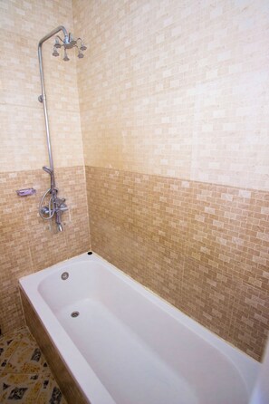 A bathroom with a white bathtub, a showerhead, and a tiled wall. - Peace of Mind Resthouse (Mbeya)