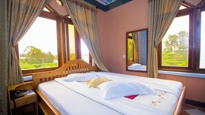 Ein ordentlich bezogenes Bett mit weißen Leinentextilien und einem floralen Muster, ein Holz-Kopfteil und ein Nachttisch mit Telefon.